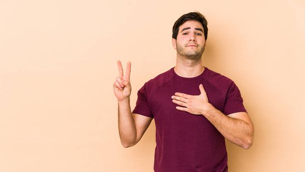 Young man isolated on beige background taking an oath, putting hand on chest. - Photo, Image