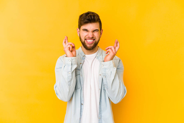 Giovane uomo caucasico isolato su sfondo giallo incrociando le dita per avere fortuna - Foto, immagini