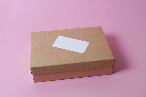 Картонная коробка с крышкой на розовом фоне сверху. Понятие доставки, почты, судеб, карантинного периода имеет значение. Принято. Доставка визитной карточки с местом для текста. - Фото, изображение