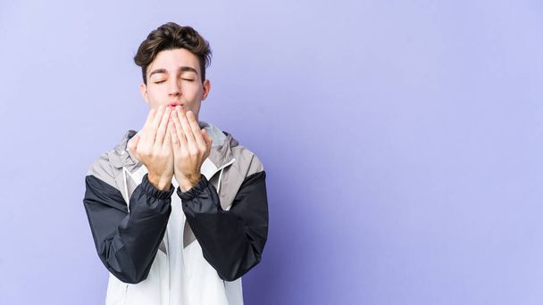 Jonge blanke man geïsoleerd op paarse achtergrond vouwen lippen en handpalmen om lucht te kussen sturen. - Foto, afbeelding