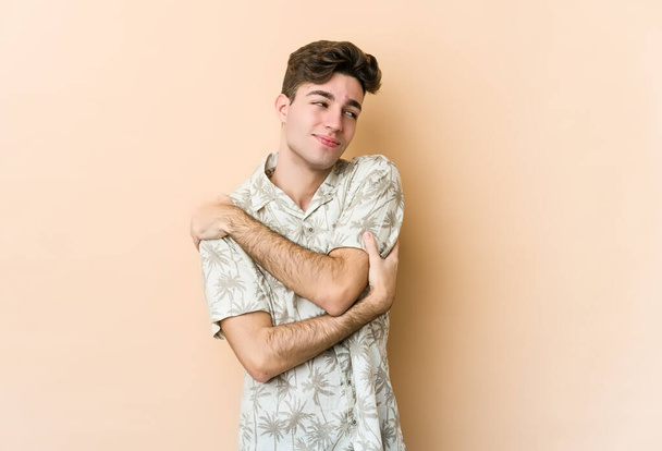 Young caucasian man isolated on beige background hugs, smiling carefree and happy. - Photo, Image