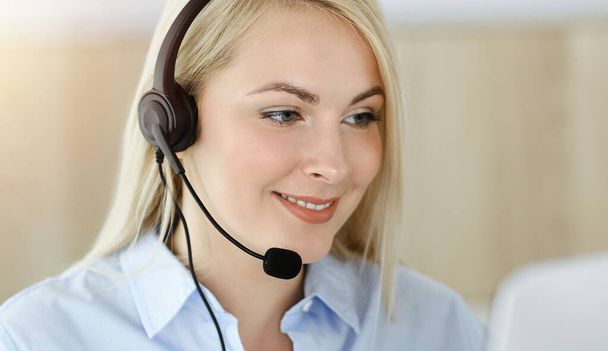 Blonde business woman sitting and communicated by headset in call center in sunny office. Concept of telesales business - Foto, Bild
