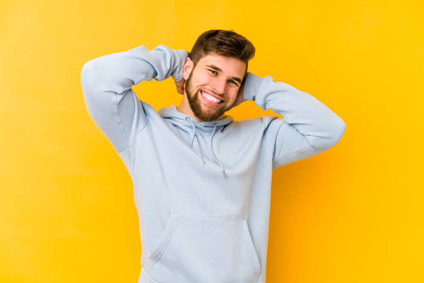Young caucasian man isolated on yellow background stretching arms, relaxed position. - Photo, Image