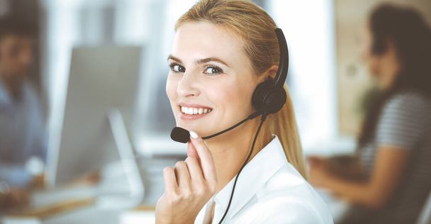 Blonde business woman using headset for communication and consulting people at customer service office. Call center. Group of operators at work - Valokuva, kuva