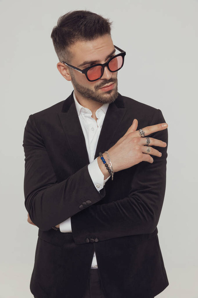 Curious fashion model pointing away and wearing sunglasses while standing on gray studio background - Φωτογραφία, εικόνα