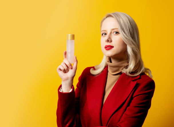 woman in red coat with lotion bottle on yellow background - Fotó, kép