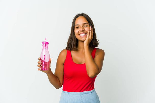 Young latin woman holding a milkshake isolated on white background holds copy space on a palm, keep hand over cheek. Amazed and delighted. - Foto, Imagem
