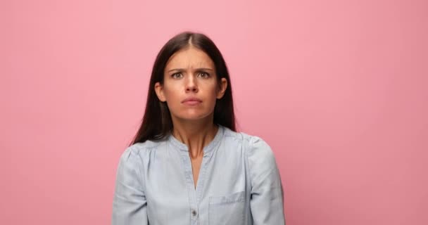 hyperaktiivinen rento nainen sinisessä denim-paidassa, joka tekee hauskoja kasvoja, toimii järkyttyneenä, huutaa ja tekee käsieleitä vaaleanpunaisella taustalla - Materiaali, video