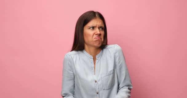 young casual woman in blue denim shirt having a superior attitude, making faces, pointing fingers to temples and inviting to think, making bla bla bla gestures, looking around and refusing on pink background - Footage, Video