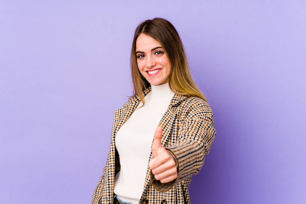 Young caucasian woman isolated on purple background smiling and raising thumb up - Photo, image