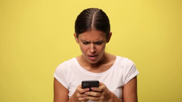 mulher casual atraente olhando para o telefone e sentindo-se enojado no fundo amarelo - Filmagem, Vídeo