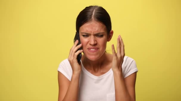 молодая случайная женщина злится на кого-то, с кем она разговаривает по телефону, кричит, жестом сумасшедший знак на желтом фоне - Кадры, видео