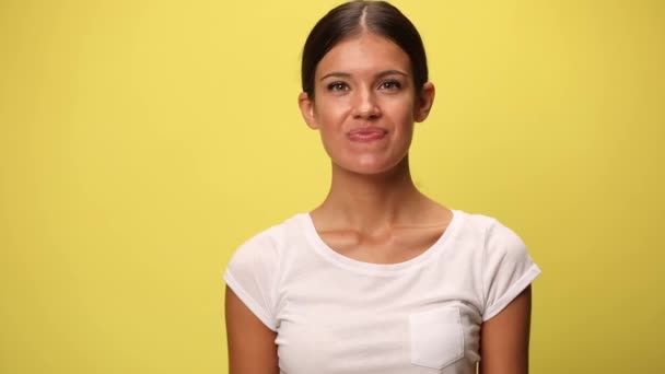 young casual woman looking down, laughing, feeling excited, dancing around and celebrating the victory on yellow background - Footage, Video