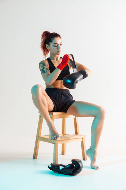 A young boxer girl with red bandages on her hands poses on a chair in a photo Studio. - Foto, imagen