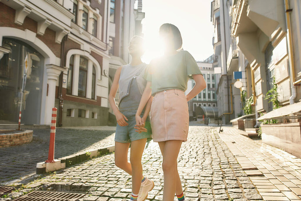 Young lesbian couple, two women in casual wear holding hands, walking along the street while exploring the city on a sunny day - Foto, imagen