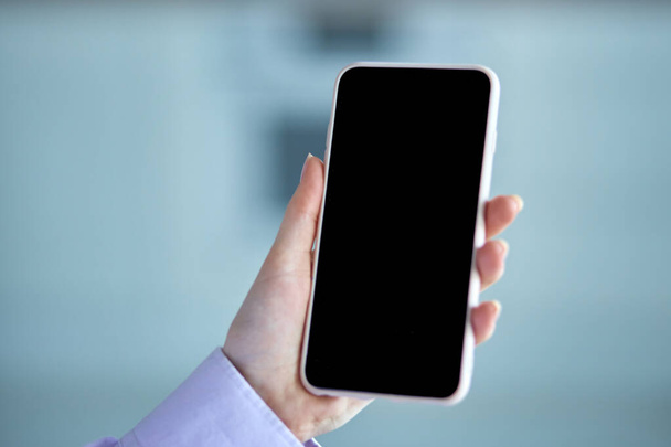 A man holds a black smartphone in his hand, against a blurry background - Foto, immagini