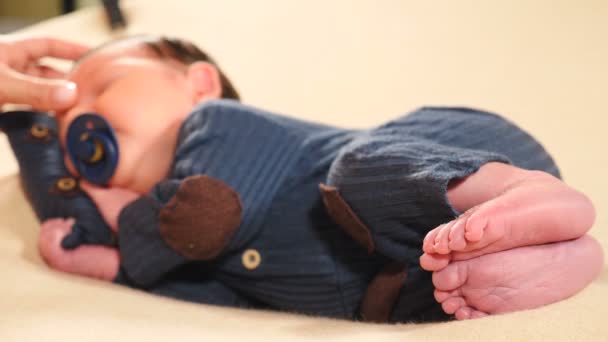 Pequeño niño recién nacido adorable con chupete acostado dormido vestido con traje de punto, mano debajo de su cabeza. Lindo niño durmiendo mientras la madre toca y acaricia su piel en la nariz y las mejillas. 4 k - Metraje, vídeo