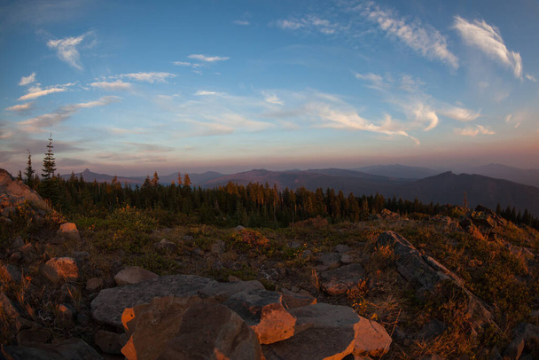 Lagen van rook van een nabijgelegen wildvuur geven een oranje gloed aan de ondergaande zon over de Cascade Mountains gezien vanaf de top van de Red Blanket Mountain bij Prospect, Oregon. - Foto, afbeelding