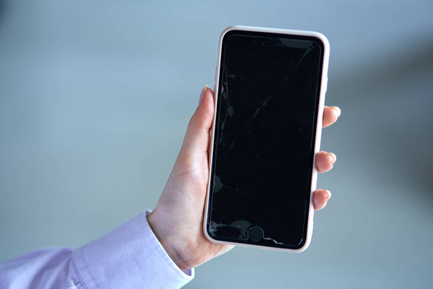 Close-up of a phone with a broken screen on a blue blurry background. - Foto, imagen