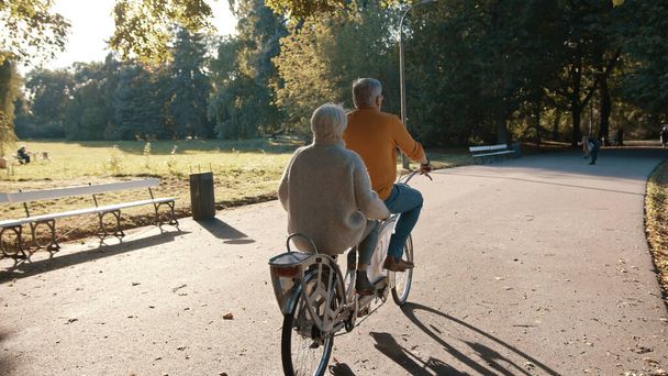 Seniorenpaar rijden dubbele fiets in de herfst. Grootmoeder en grootvader fietsen samen. Ouderen gezonde en actieve levensstijl. - Foto, afbeelding