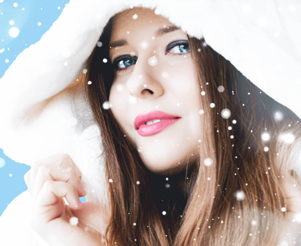 Рождественский и зимний праздничный портрет молодой женщины в белой шубе в капюшоне, снег на синем фоне, мода и стиль жизни - Фото, изображение