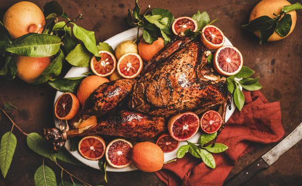 Christmas or Thanksgiving Day festive table setting. Whole roasted turkey with citrus fruit over rusty table background, top view, selective focus. Holiday gathering food concept - Valokuva, kuva