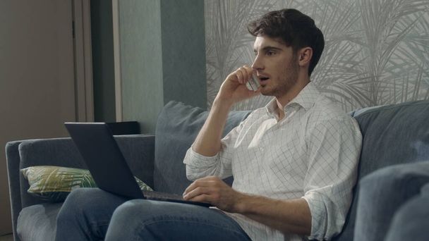 Pewny siebie człowiek korzystający jednocześnie z telefonu na laptopie. Facet pracujący z komputerem smartfona - Zdjęcie, obraz