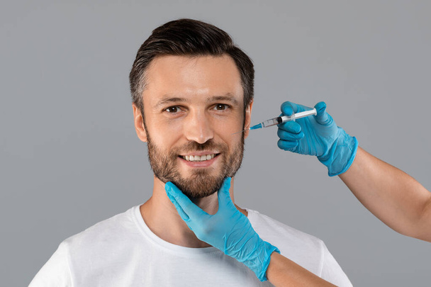 Cosmetician injecting face filler for middle-aged man - Fotoğraf, Görsel