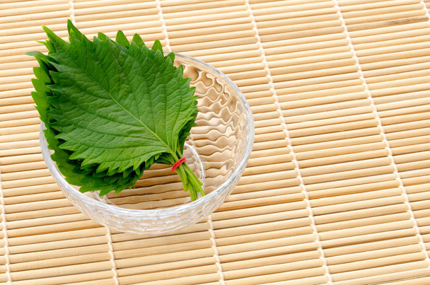 Friss zöld Shiso (perilla frutescens) vagy Oba levél egy kis átlátszó üveggömb alakú tálban bambusz guruló szőnyegen. - Fotó, kép