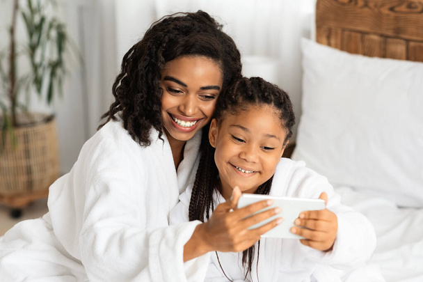słodkie mało czarny dziewczyna i jej mama w szlafroki biorąc Selfie razem - Zdjęcie, obraz