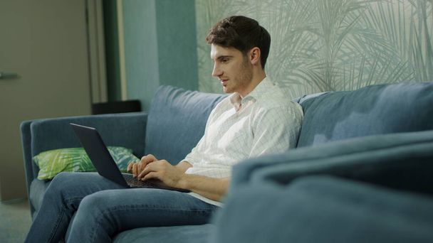 Vrolijke man met een computer in het hotel. Knappe jongen leest bericht op laptop. - Foto, afbeelding