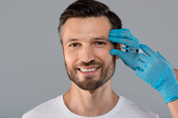 Happy man getting anti-wrinkle injection in eye zone - Foto, immagini
