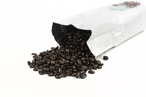 Paahdettuja kahvipapuja vuotaa pussista, jossa on värillinen kuvio. Valkoinen / valkoinen - Valokuva, kuva
