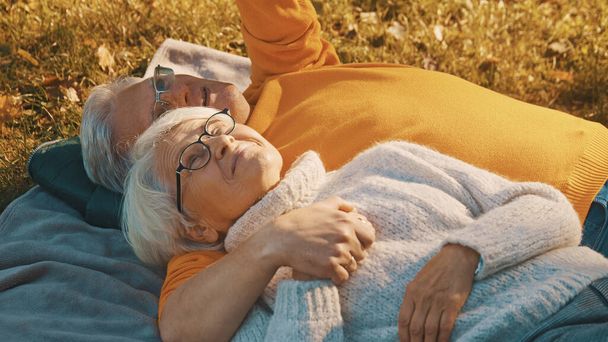 古い時代のロマンス。公園で秋の日を楽しむ退職者のカップル。毛布の上に横になり、お互いを見て - 写真・画像