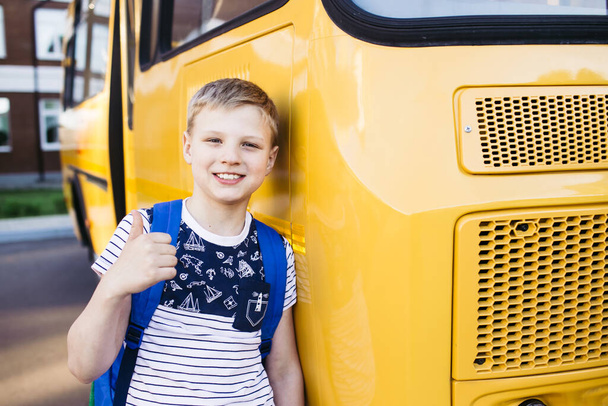 Smiling School Boy from elementary school shows a thumbs up in front of school bus. Back to school. Education. Day of knowledge. - Foto, afbeelding