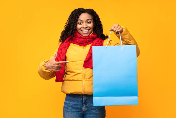 陽気なアフリカの女性ショッピングバッグで指を指す、黄色の背景 - 写真・画像