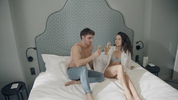 Una coppia sorridente che beve champagne a letto. Hot coppia guardando l'un l'altro in casa. - Foto, immagini