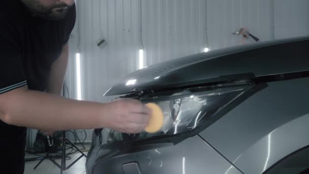 Car detailing. Polisher applies special polishing compound or paste or wax to optics of car headlight with sponge, close up - Footage, Video