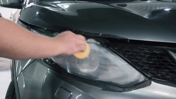 Detallando el coche. Pulidor aplica compuesto de pulido especial o pasta o cera a la óptica del faro del coche con esponja, de cerca - Metraje, vídeo