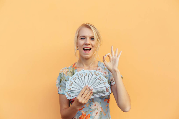Portrait beautiful young woman with money and cash on orange pastel isolated background - Photo, Image