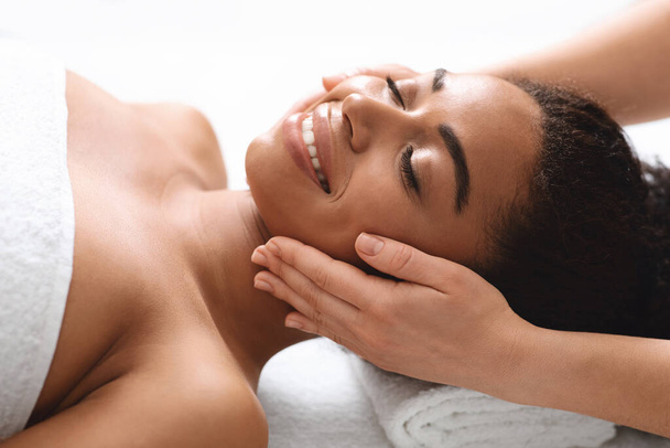 Усміхнена чорна жінка має масаж обличчя в спа-салоні
 - Фото, зображення