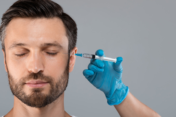 Bärtiger Mann mittleren Alters bekommt Anti-Falten-Injektion in die Augenzone - Foto, Bild
