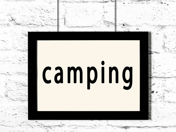 Black frame hanging on white brick wall with inscription camping - Photo, Image