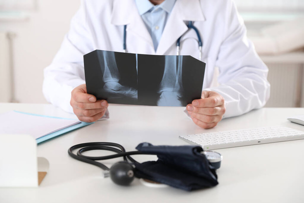 Orthopedist examining X-ray picture at desk in office, closeup - Photo, Image