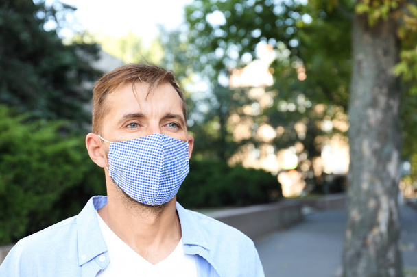 Man wearing handmade cloth mask outdoors, space for text. Personal protective equipment during COVID-19 pandemic - Foto, Imagem