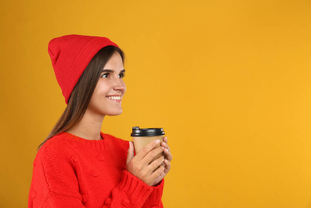 Happy beautiful woman with paper cup of mulled wine on yellow background. Space for text - Фото, зображення