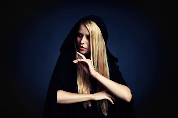 Witch in black mantle on dark background. Scary fantasy character - Photo, image