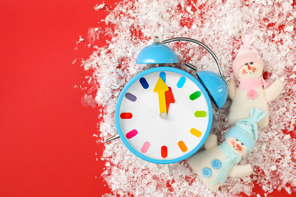 Alarm clock and snowmen in pile of snow on red background, flat lay with space for text. New Year countdown - Fotó, kép