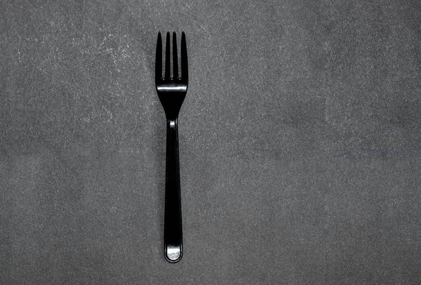 egyszerű tiszta fekete műanyag villa lapos, tiszta szürke háttéren kemény árnyékkal. Az ételek minimalista monokróm fotója. - Fotó, kép