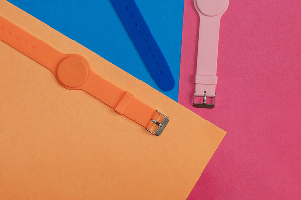 Πορτοκαλί, μπλε και ροζ ρολόι σιλικόνης με μαγνητικό αισθητήρα σε πορτοκαλί καθαρό φόντο. Μονόχρωμη εικόνα. Υγιεινός τρόπος ζωής, παρακολουθεί την υγεία σας - Φωτογραφία, εικόνα
